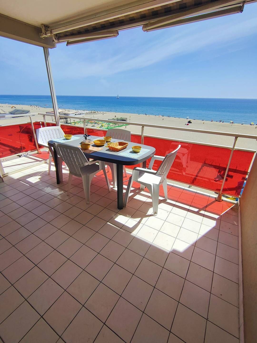 A balcony with a table and chairs, overlooking a beach with a clear sky.