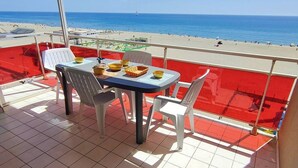 A balcony with a table and chairs, overlooking a beach with a clear sky. - Appartement T2 vue Mer, Moderne, Clim 3 Etoiles Parking 4plmer53 (CANET PLAGE)