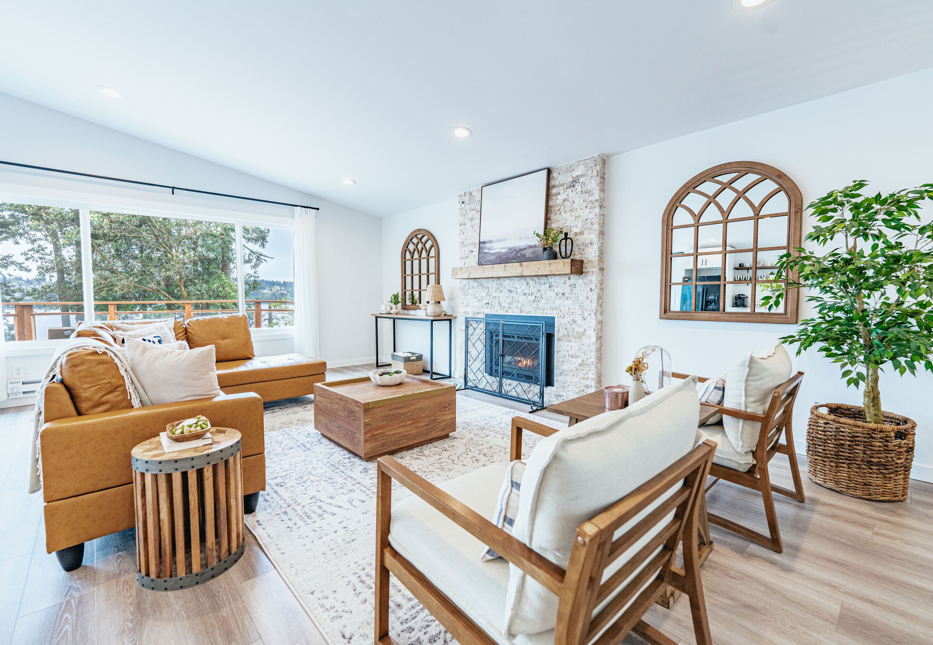 A spacious living room with a fireplace, wooden furniture, and large windows offering a view of the outdoors.