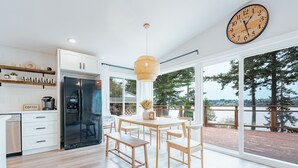 Una cocina moderna con refrigerador empotrado, mesa de comedor de madera y sillas. Hay un ventanal con vistas a árboles y una terraza.
