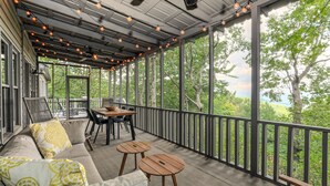 A covered porch with a sofa, two wooden tables, and a dining table.
