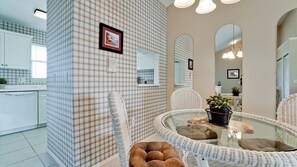 A modern kitchen with white cabinetry, a checkered backsplash, and a dining area with wicker furniture and a glass table.