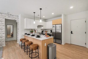Une cuisine moderne avec des meubles blancs, un îlot central doté de tabourets, des appareils en acier inoxydable et un éclairage suspendu.