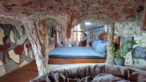 Una habitación rústica con una pared de piedra, una cama y una planta colgante.