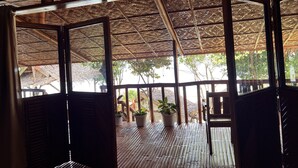 Un espacio al aire libre cubierto con piso de bambú y techo, barandillas de madera y plantas en macetas.
