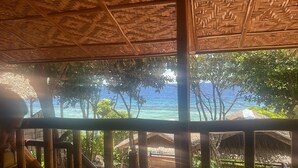 Una habitación con vistas al océano, techo de paja y barandilla de madera.