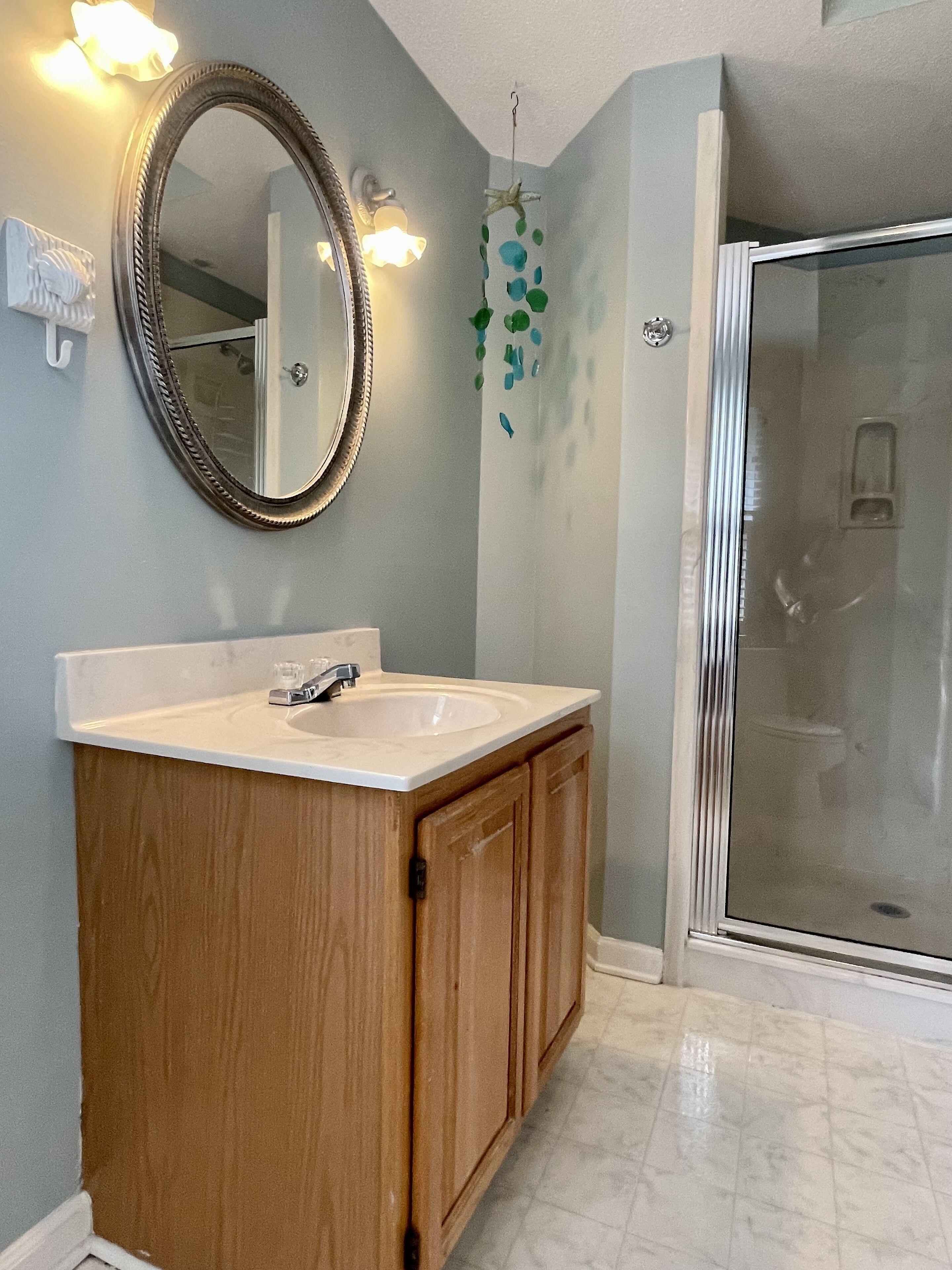 A bathroom with a wooden vanity, a round mirror, a sink, and a glass shower enclosure.