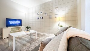 Uma sala de estar moderna com televisão de tela plana, mesa de centro branca, sofá e luminária fixa na parede.
