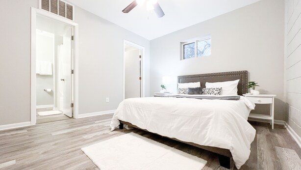 Quarto com cama, mesa de cabeceira, ventilador de teto e janela.