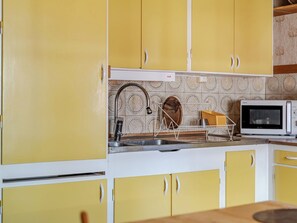 A kitchen with yellow cabinets, a stainless steel sink, and a white microwave.