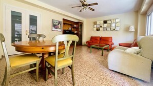 A living room with a dining table, chairs, a sofa, a coffee table, and a ceiling fan.