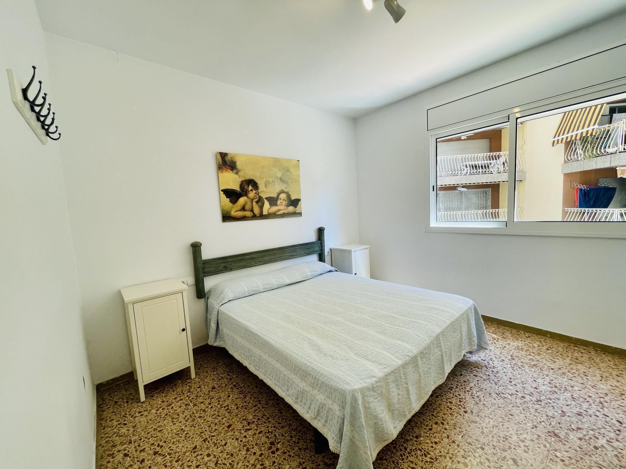 A bedroom with a bed, a nightstand, a painting, a wardrobe, and a window with a balcony view.