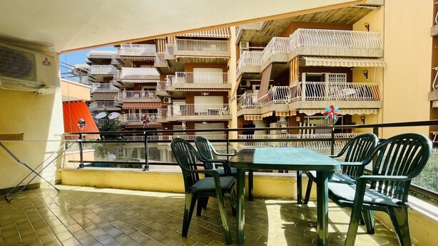 A balcony with a table and chairs, overlooking a multi-story building with balconies.