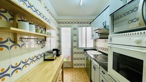 A kitchen with patterned tiles, wooden shelves, a built-in oven, and a window.