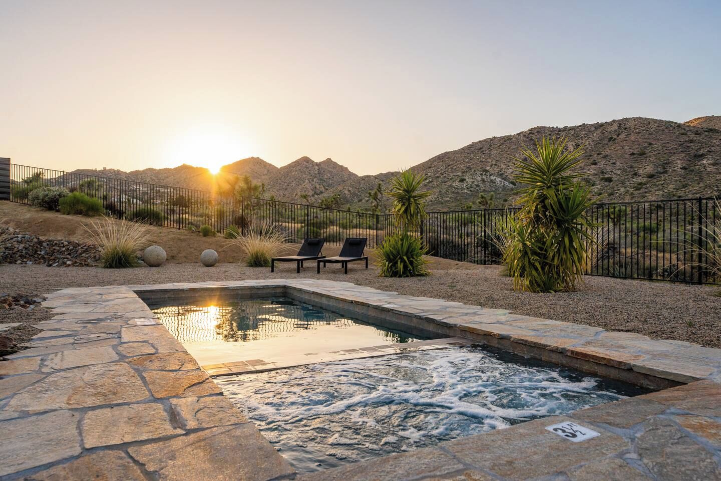 Una piscina con solárium de piedra, dos sillas de descanso y vistas a montañas al fondo.