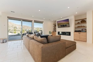 A modern living room with a large sofa, a dining table, and a kitchen area with built-in appliances.