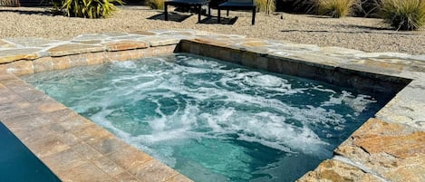 Un jacuzzi con borde de piedra, rodeado por un patio con sillas y plantas.
