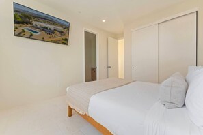 Een slaapkamer met een bed, een groot raam en een deur naar een andere kamer.