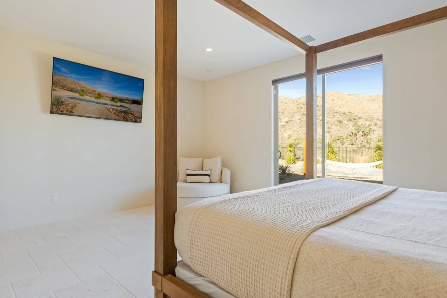 Un dormitorio con una cama grande, vistas de un paisaje desértico a través de una puerta corredera y un cuadro en la pared.