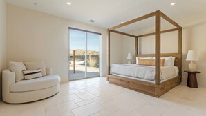 A bedroom with a four-poster bed, a sofa, and a sliding glass door leading to an outdoor area. - Stardust Luxe - Modern Desert Retreat - Heated Pool, Spa & Firepit (Yucca Valley)