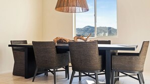 A dining area with a table and chairs, a hanging light fixture, and a view of mountains through a window.