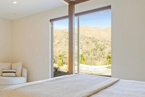 A bedroom with a large bed, a sofa, and a sliding glass door leading to a desert view.