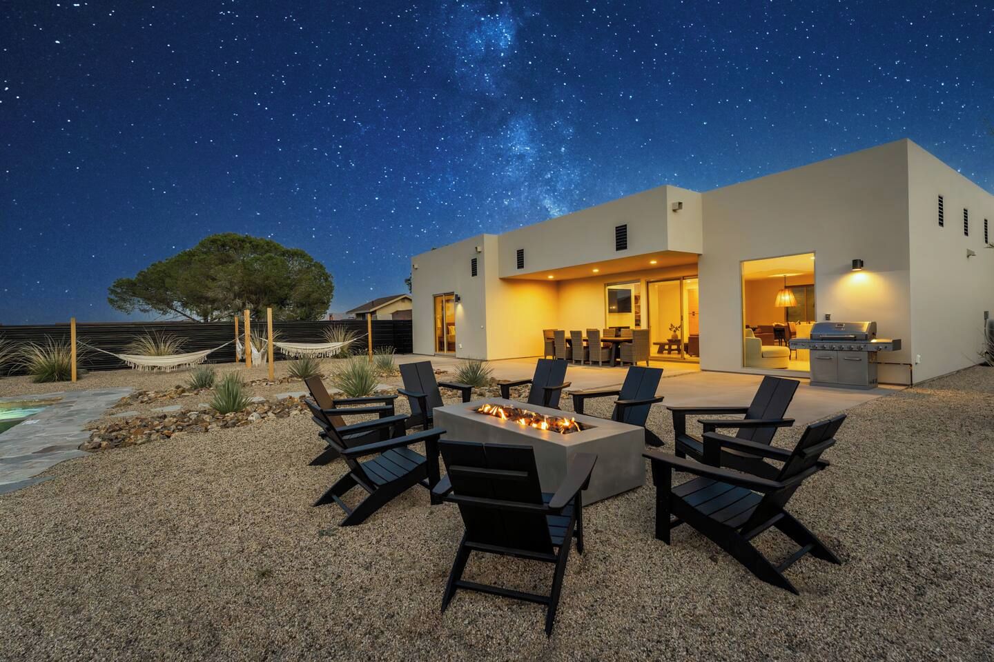 A modern house with a patio area featuring outdoor seating and a fire pit, under a starry night sky.