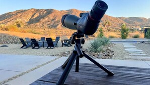 A telescope on a tripod in an outdoor setting with chairs and a mountainous background. - Stardust Luxe - Modern Desert Retreat - Heated Pool, Spa & Firepit (Yucca Valley)