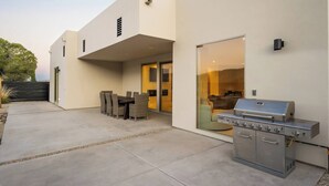 A modern outdoor patio with a grill, dining table, and chairs.