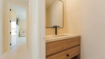 A bathroom with a wooden vanity, a mirror, and a white door leading to a living area.