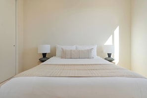 A neatly made bed with white bedding and two bedside lamps.