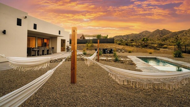 A modern outdoor setting with a pool, a hammock, and a building with outdoor seating. - Stardust Luxe - Modern Desert Retreat - Heated Pool, Spa & Firepit (Yucca Valley)