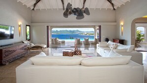 Ein geräumiges Wohnzimmer mit einem großen, weißen Sofa, einem Fernseher und Blick auf das Meer.
