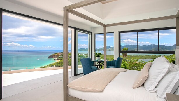 Een slaapkamer met een groot bed, uitzicht op zee en een balkon met stoelen.