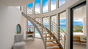 Een modern interieur met een gebogen trap die leidt naar een balkon met uitzicht op de kust.