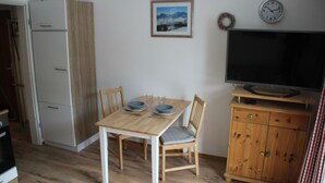 Une cuisine de taille réduite comprenant une table à manger, des chaises, un réfrigérateur, un téléviseur et un meuble en bois.