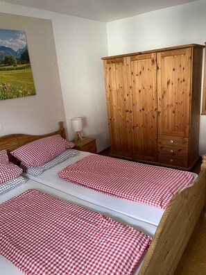 Une chambre avec deux lits, une armoire en bois, une table de chevet et un tableau au mur.