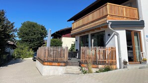 Une maison moderne dotée d’un balcon en bois, d’une allée pavée et surplombée d’un ciel bleu azur.