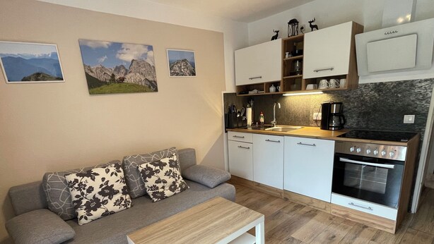 Un espace de vie compact comprenant un canapé, une petite table, une kitchenette avec une cuisinière et des placards fixés au mur.