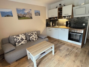 Un espace de vie compact comprenant un canapé, une petite table, une kitchenette avec une cuisinière et des placards fixés au mur.