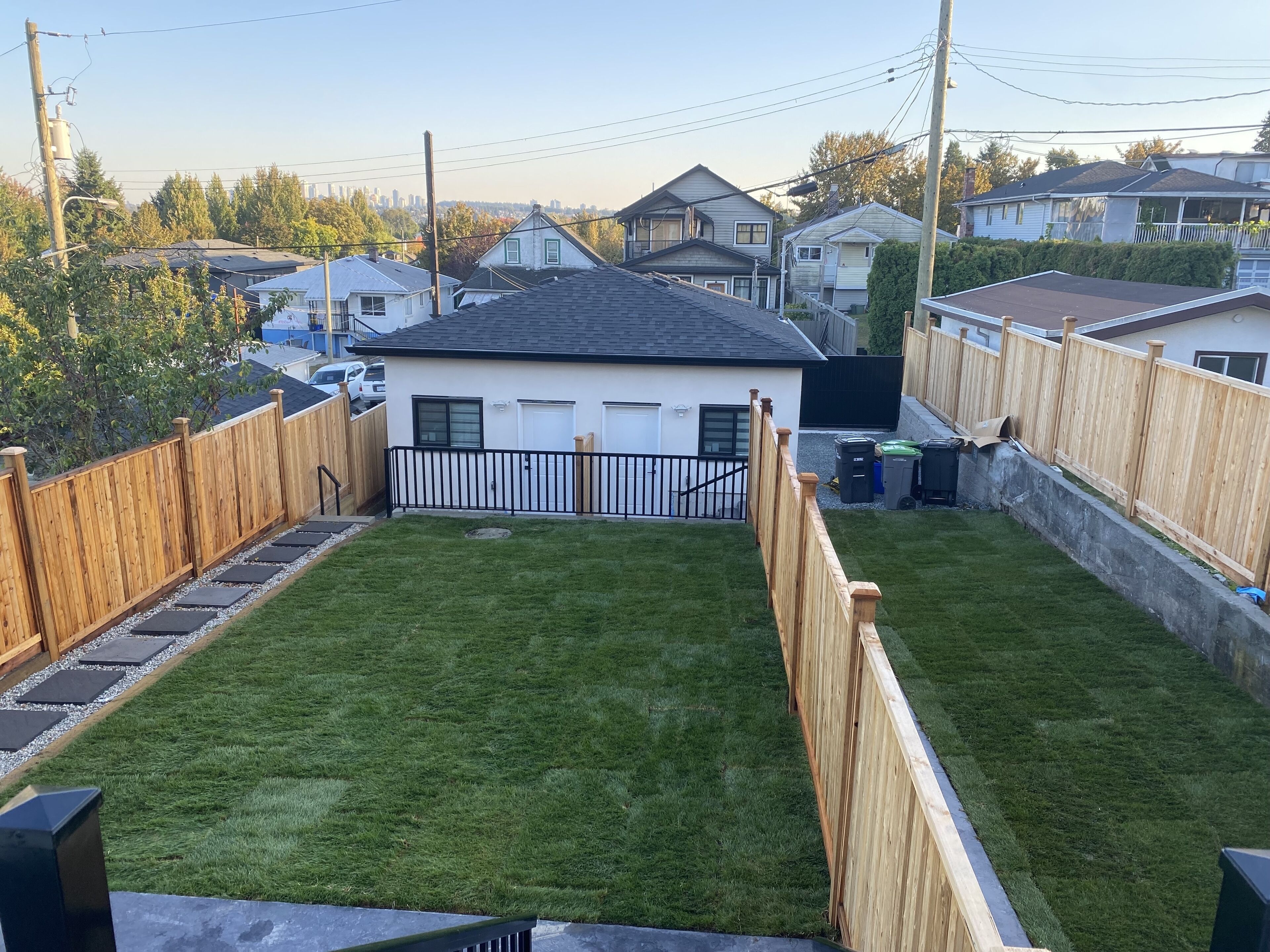 A fenced backyard with a grassy lawn, a white garage, and a wooden fence.