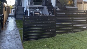 Ett modernt hus i två våningar med en fasad av sten, en täckt uteplats och en inhägnad trädgård.