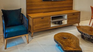 A modern living room with a wooden entertainment unit, a flat-screen TV, a blue armchair, and a coffee table. - Chill House (Cruz)