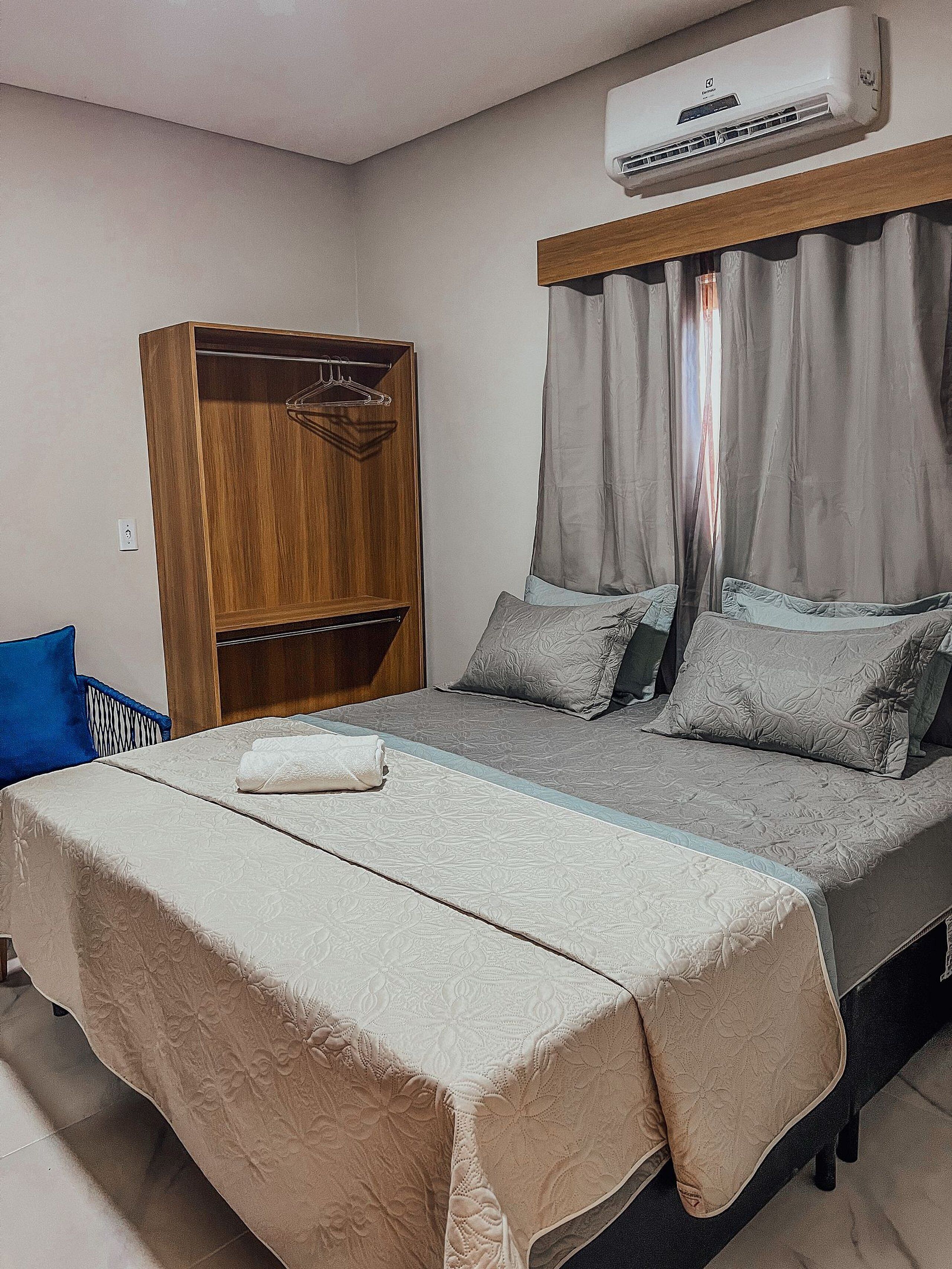 A bedroom with a bed, a wooden wardrobe, and an air conditioning unit.