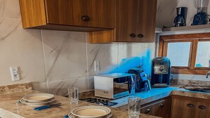 A kitchen with a marble countertop, wooden cabinets, and a coffee maker. - Chill House (Cruz)
