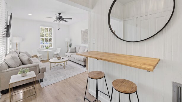 Un salon moderne avec un tabouret de bar en bois, un miroir rond et un ventilateur de plafond.