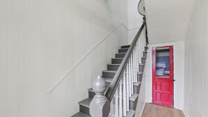 Un escalier avec des murs blancs et une porte rouge en bas.