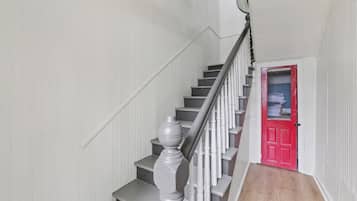 A staircase with white walls and a red door at the bottom.