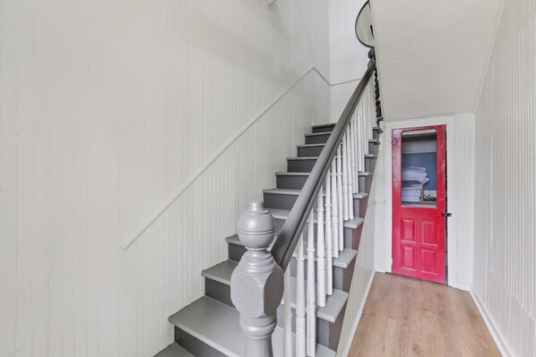 A staircase with white walls and a red door at the bottom.