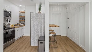 Une cuisine moderne avec des meubles blancs, un four à micro-ondes, un four en acier inoxydable, des plans de travail en bois et un dosseret décoré d’un motif en chevrons.